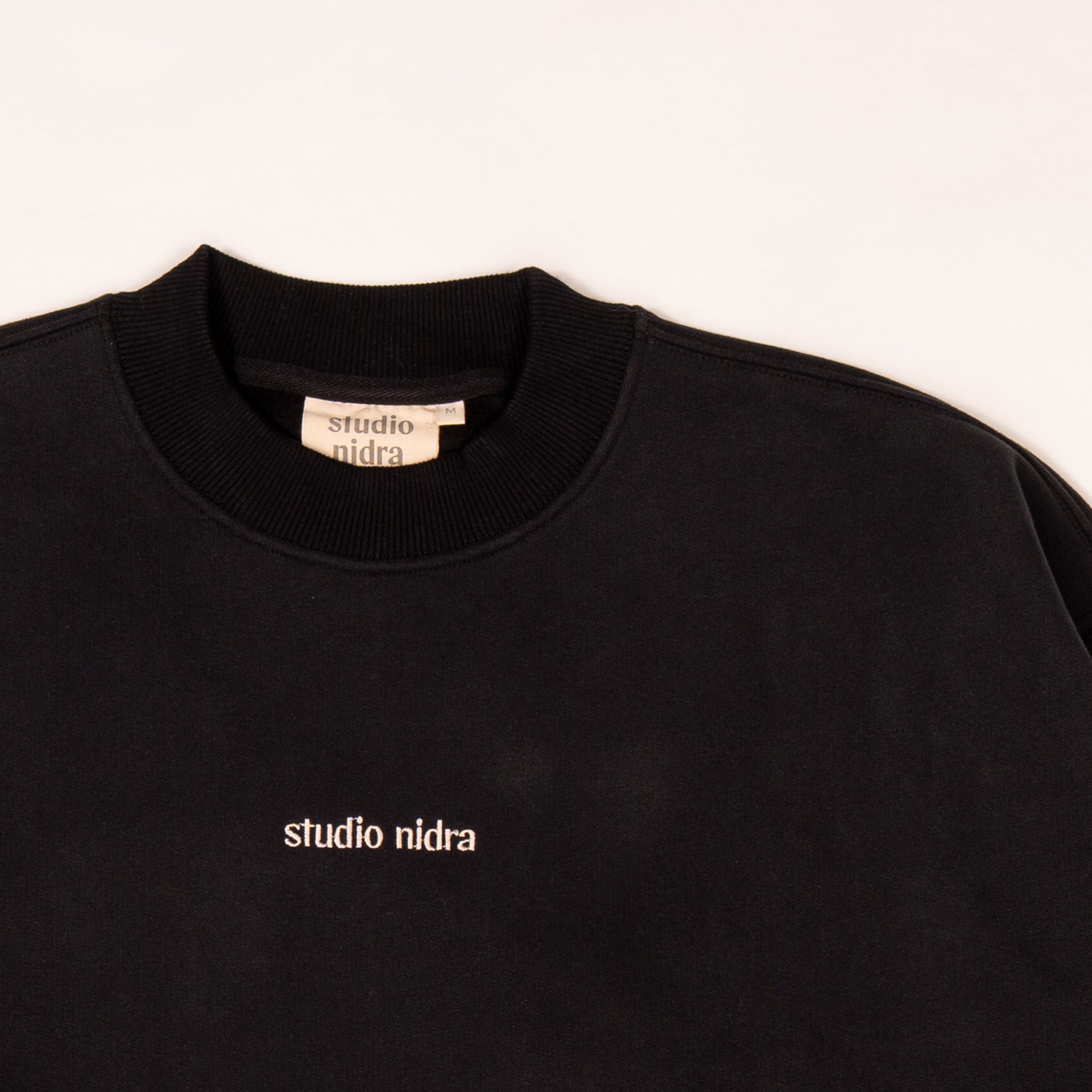 Close-up of The Crew Sweatshirt Midnight Black - peach finish texture, seams and Studio Nidra embroidery detail.
